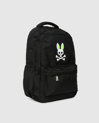 A black Psycho Bunny KIDS BACKPACK - B0A175D200 is displayed against a plain background. It features a front pocket adorned with a graphic of a cartoon bunny skull with crossbones, where the bunny's ears are highlighted in green and white. This smaller graphic is also depicted at the bottom of the front pocket. The adjustable shoulder straps ensure comfort and customizable fit for all users.