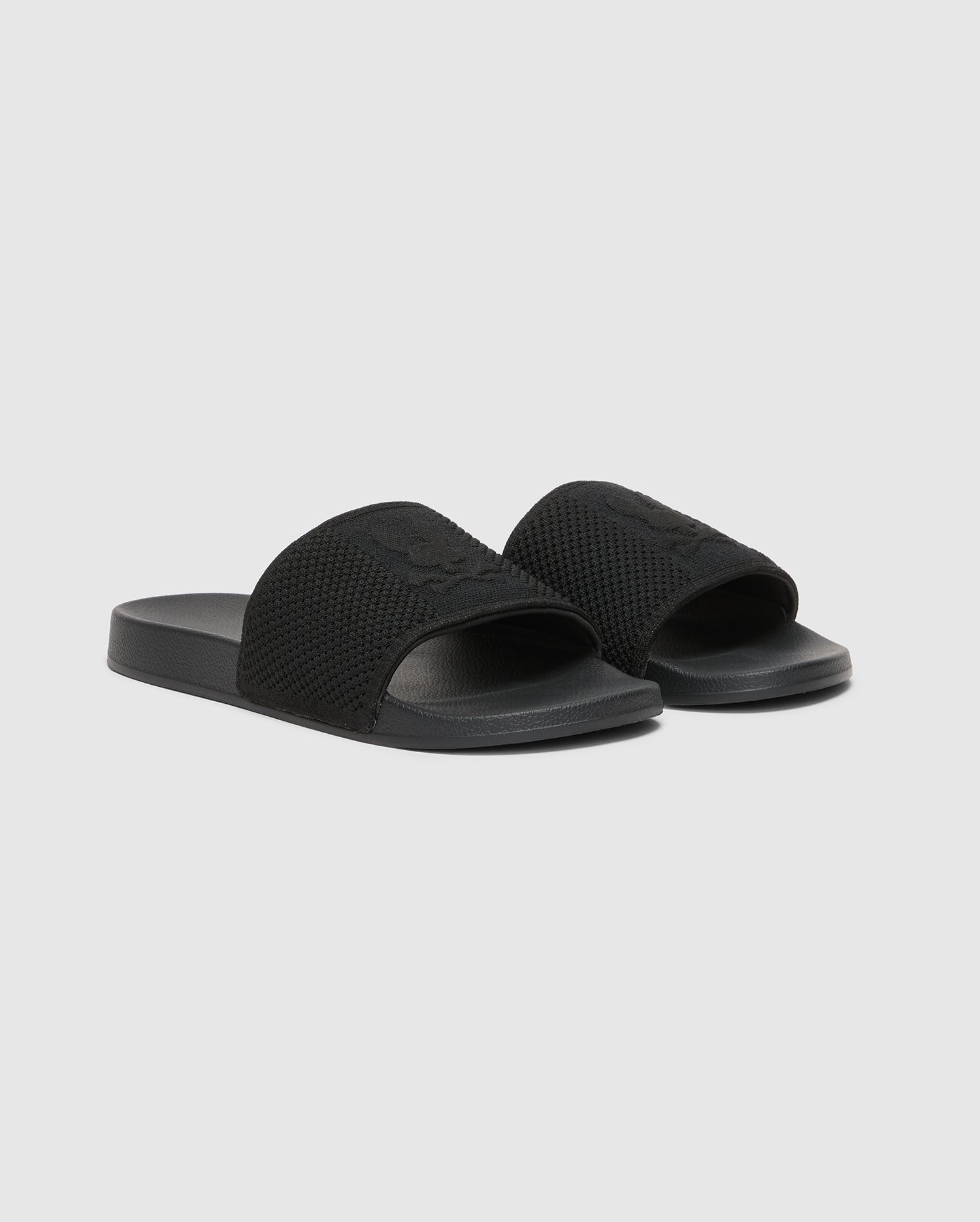 The Psycho Bunny KIDS KNIT SLIDES (B0A377F200) are black slide sandals with textured straps. They feature flat soles, open toes, a molded footbed, and subtle strap design for comfort, all set against a light gray background.