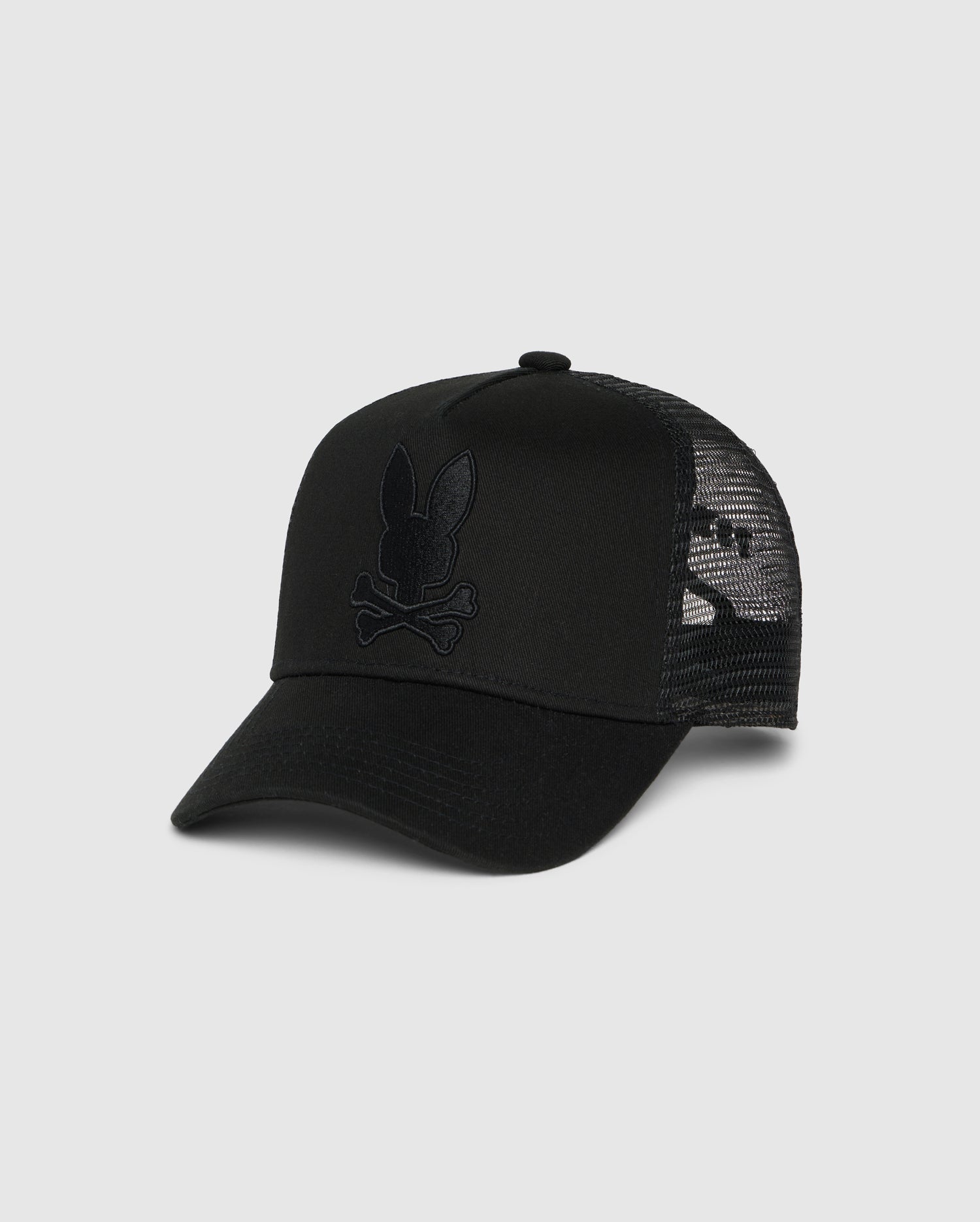 A black trucker hat with a mesh back and an emblem featuring a rabbit skull and crossbones design on the front, complete with snapback fastening for the perfect fit, is the KIDS HOUSTON TRUCKER HAT - B0A550C2HT by Psycho Bunny.