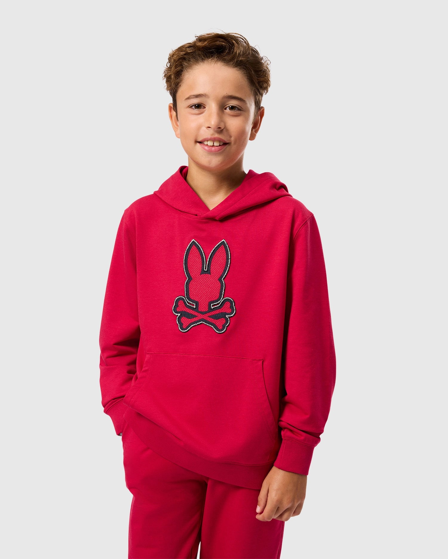 A boy wearing the Psycho Bunny KIDS WALTER LIGHTWEIGHT HOODIE - B0H476D200 in red, crafted from modern Micro French terry fabric.