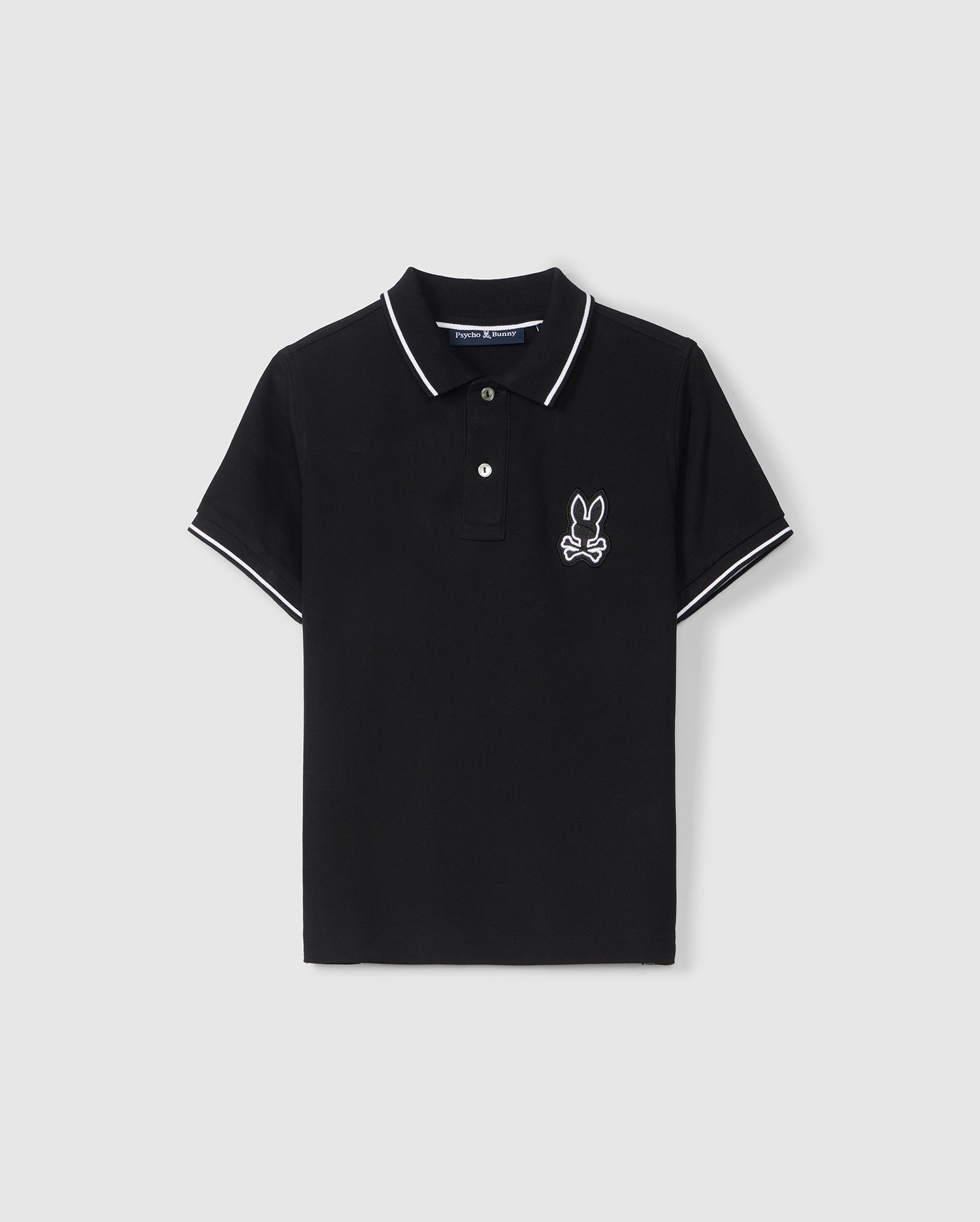 A black short-sleeve KIDS LENOX PIQUE POLO SHIRT - B0K138B200 with white trim on the collar and sleeves. Made from soft Pima cotton, it features a small embroidered bunny with crossed bones near the left chest area by Psycho Bunny.