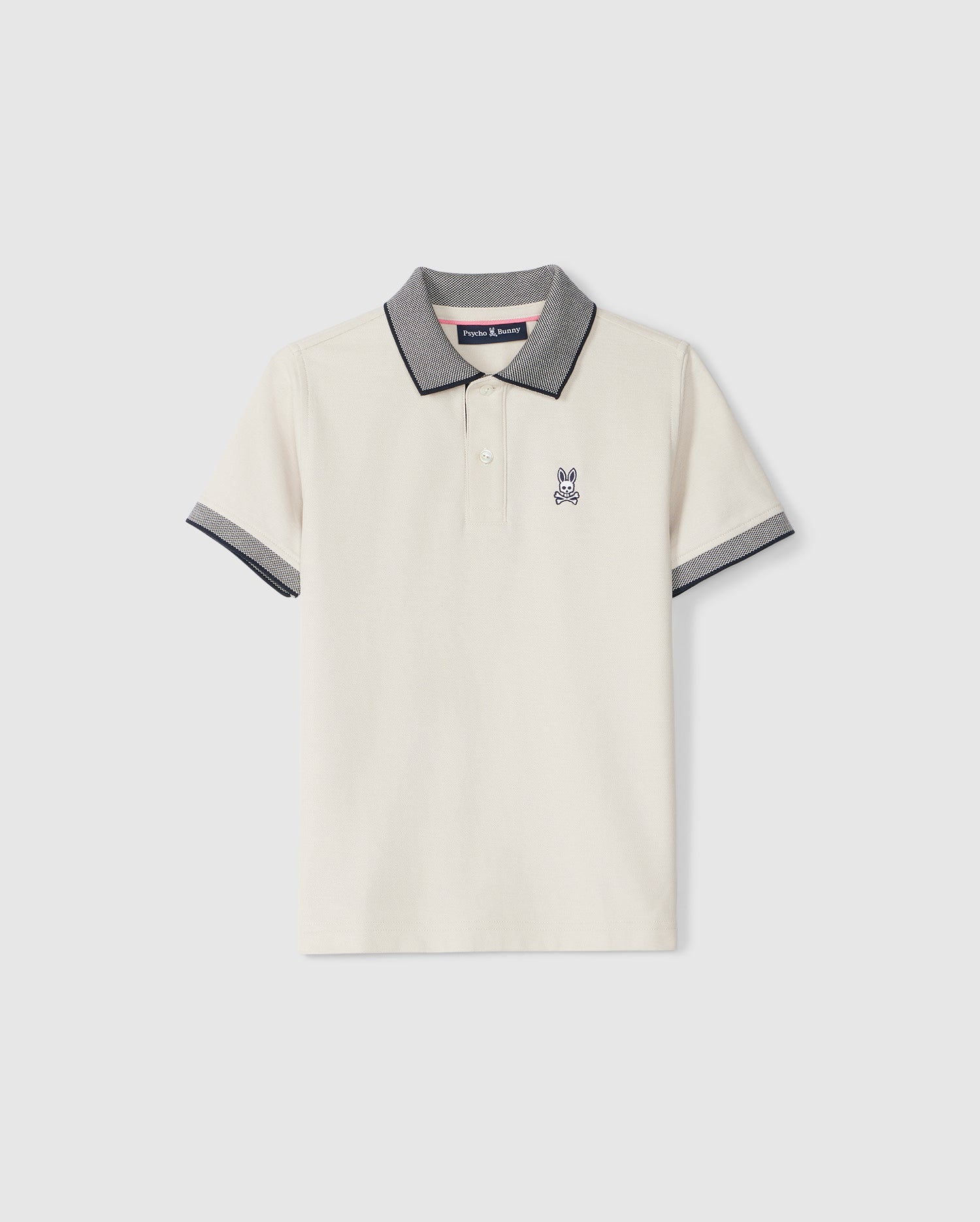 A light beige KIDS SOUTHPORT PIQUE POLO SHIRT - B0K263B200 by Psycho Bunny in Pima cotton piqué with dark grey trim on the collar and sleeves. The shirt features a small embroidered logo of a rabbit on the left chest. This stylish polo has a three-button placket and is displayed against a plain white background.