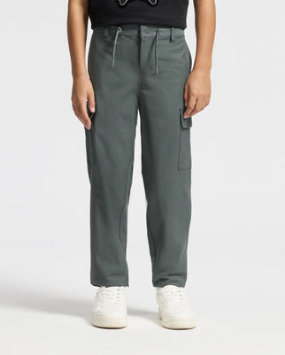 A person wearing the trendy KIDS GREEN VALLEY CARGO PANT by Psycho Bunny, featuring a drawstring waist and multiple pockets, paired with a black shirt and white sneakers. The plain white background highlights this stylish ensemble.