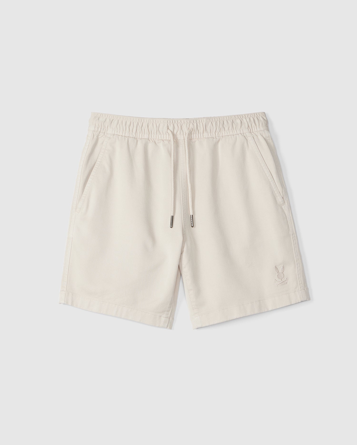 A pair of beige men's KIDS WILLIS STRETCH TENCEL shorts made by Psycho Bunny, with an elastic waistband and drawstrings, featuring a small embroidered logo near the bottom left hem, displayed on a plain white background.