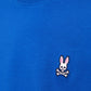 A close-up of an individual wearing the Psycho Bunny KIDS CLASSIC CREW NECK TEE in blue Pima cotton, adorned with a small embroidered design of a white rabbit skull with pink ears above crossed bones on the chest.