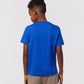 A child with short hair is seen from behind, sporting a vibrant blue KIDS CLASSIC CREW NECK TEE by Psycho Bunny and beige pants against a plain light background.