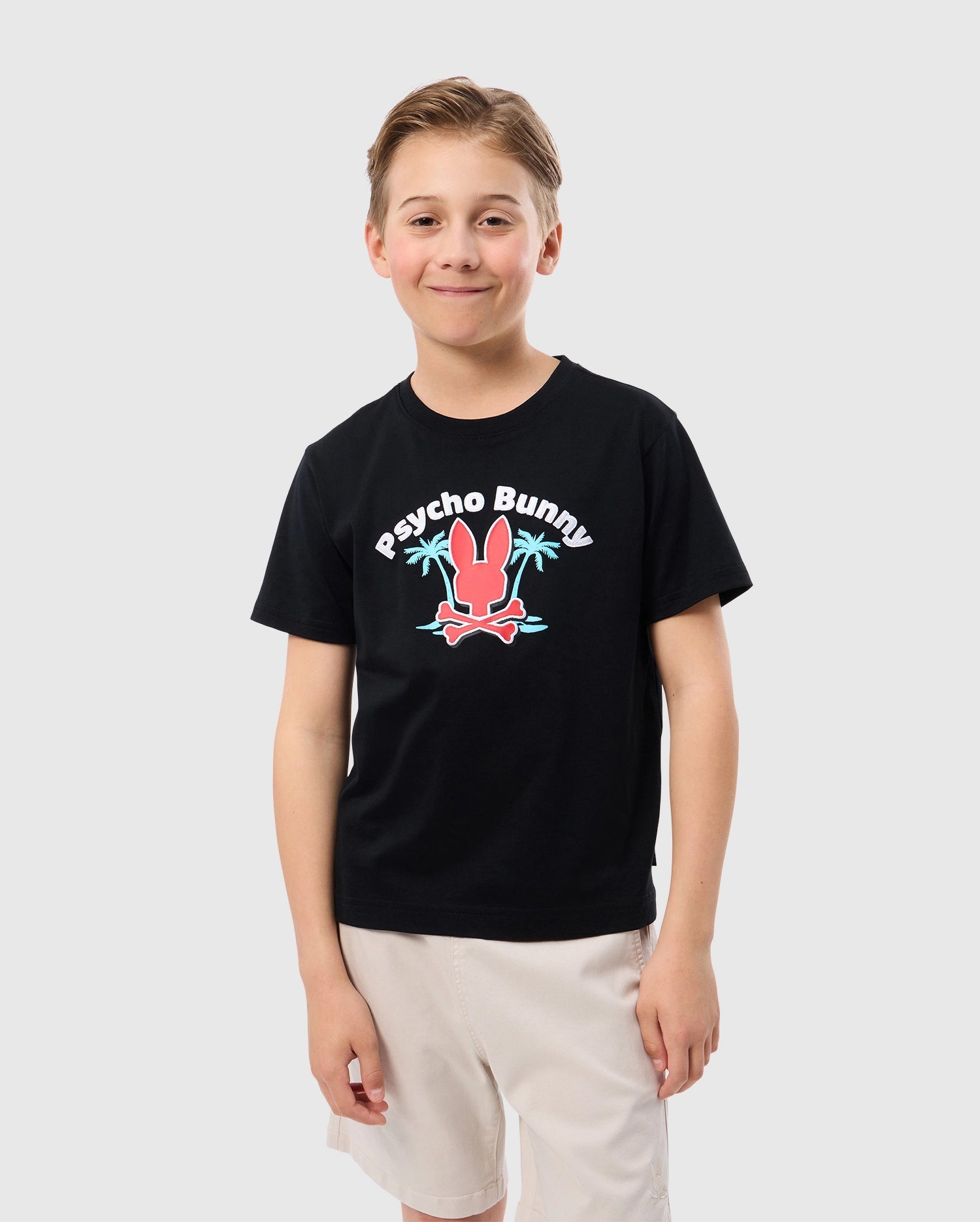 Front view of a kid model wearing the kids pima cotton boston graphic city tee in black, featuring a red psycho bunny logo, psycho bunny lettering, and two palm trees