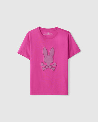 A bright pink KIDS RIVIERA GRAPHIC TEE - B0U639C200, crafted from luxurious Peruvian Pima cotton, is displayed on a plain background. The shirt features a dark pink graphic of a bunny head with crossed bones underneath, centered on the front. The neck tag indicates the brand as "Psycho Bunny.