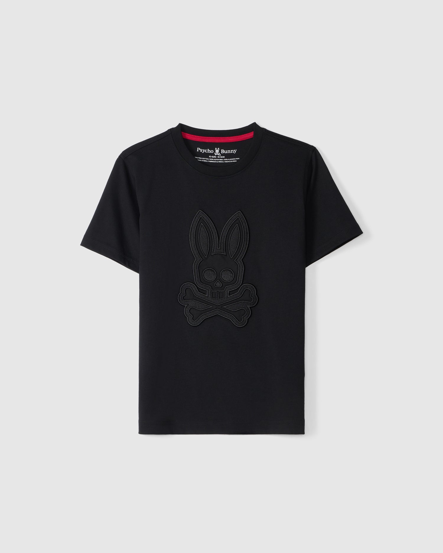 A black short-sleeve KIDS MALTON GRAPHIC TEE - B0U795D200 by Psycho Bunny features a tonal bunny skull logo prominently displayed on the front. Made from soft Pima cotton, it has a contrasting red inner trim on the neckline and a visible brand tag inside the collar. Photographed against a plain, light-colored background, this tee highlights its Peruvian craftsmanship.