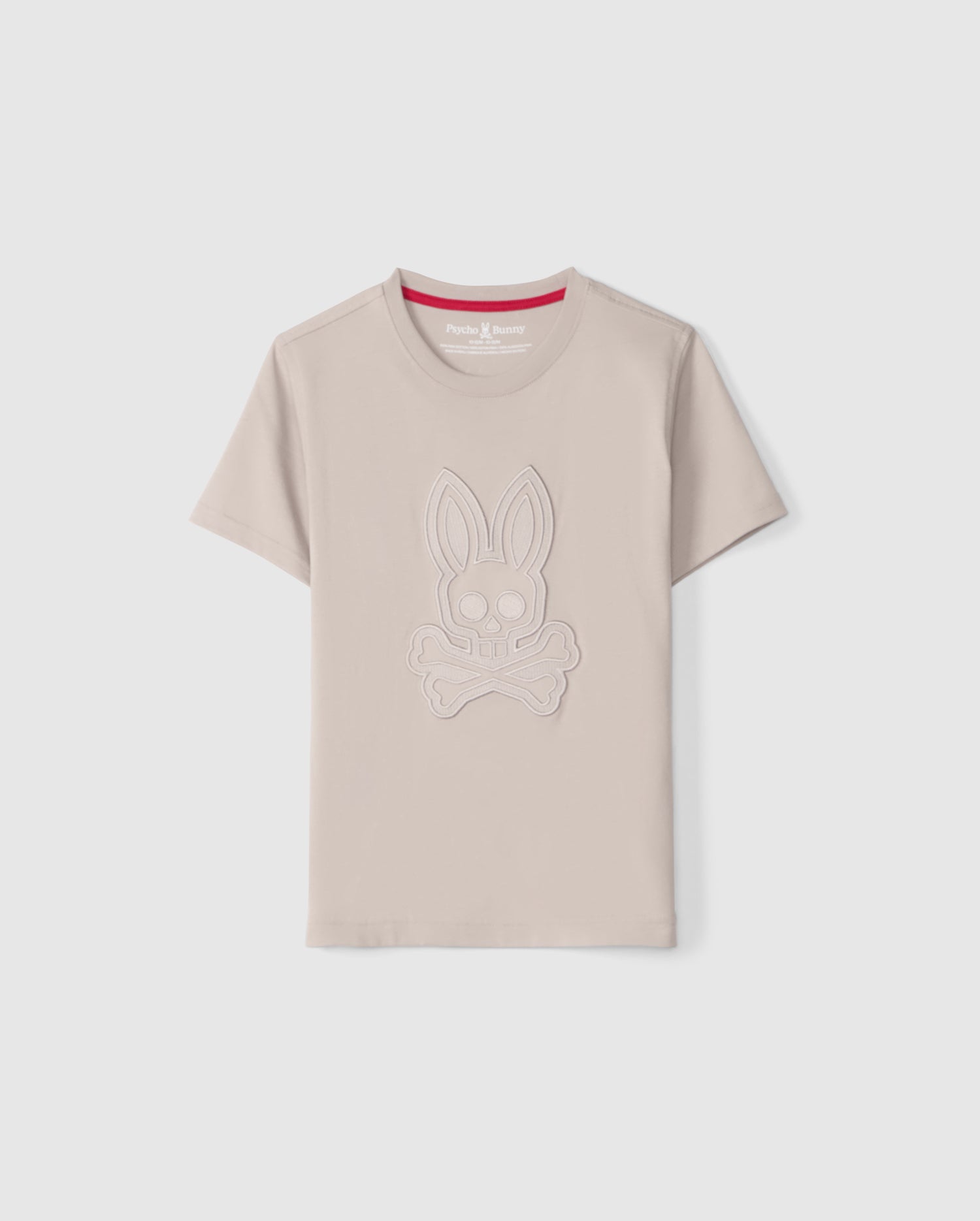 The KIDS MALTON GRAPHIC TEE - B0U795D200 from Psycho Bunny is a light beige, regular fit, short-sleeve shirt made from premium Pima cotton. It features an embossed design of a bunny's head above crossed bones and has a red inner collar with the 