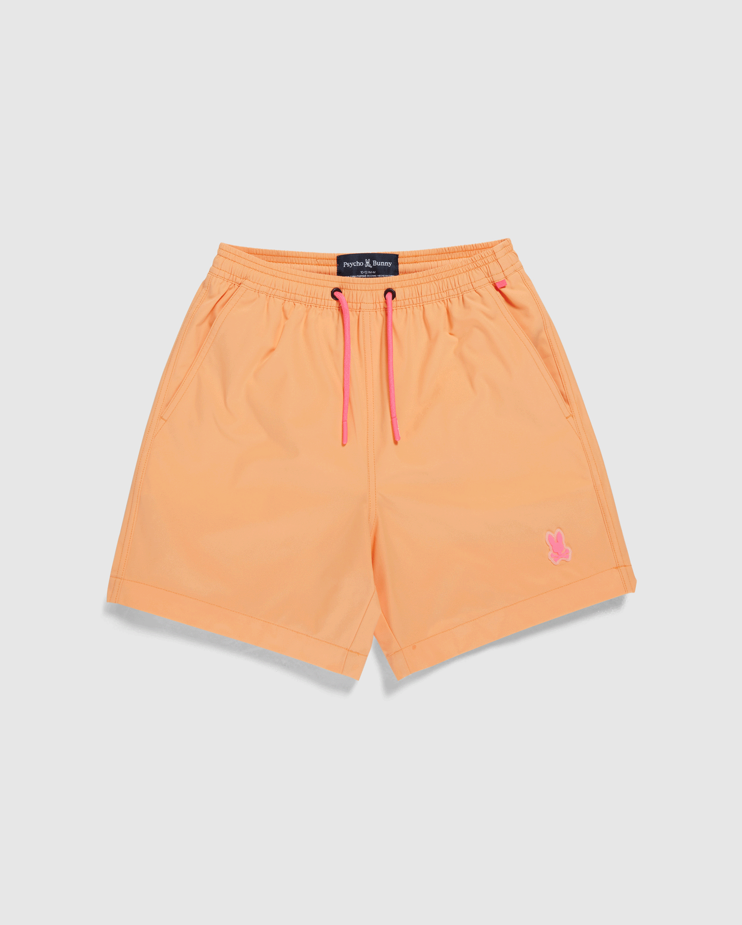 A pair of orange KIDS MALTA HYDROCHROMIC SWIM TRUNK - B0W321B2SW by Psycho Bunny with pink drawstrings at the waistband. The quick-dry material shorts have side pockets and feature a small pink bunny logo on the bottom left leg, set against a plain white background.