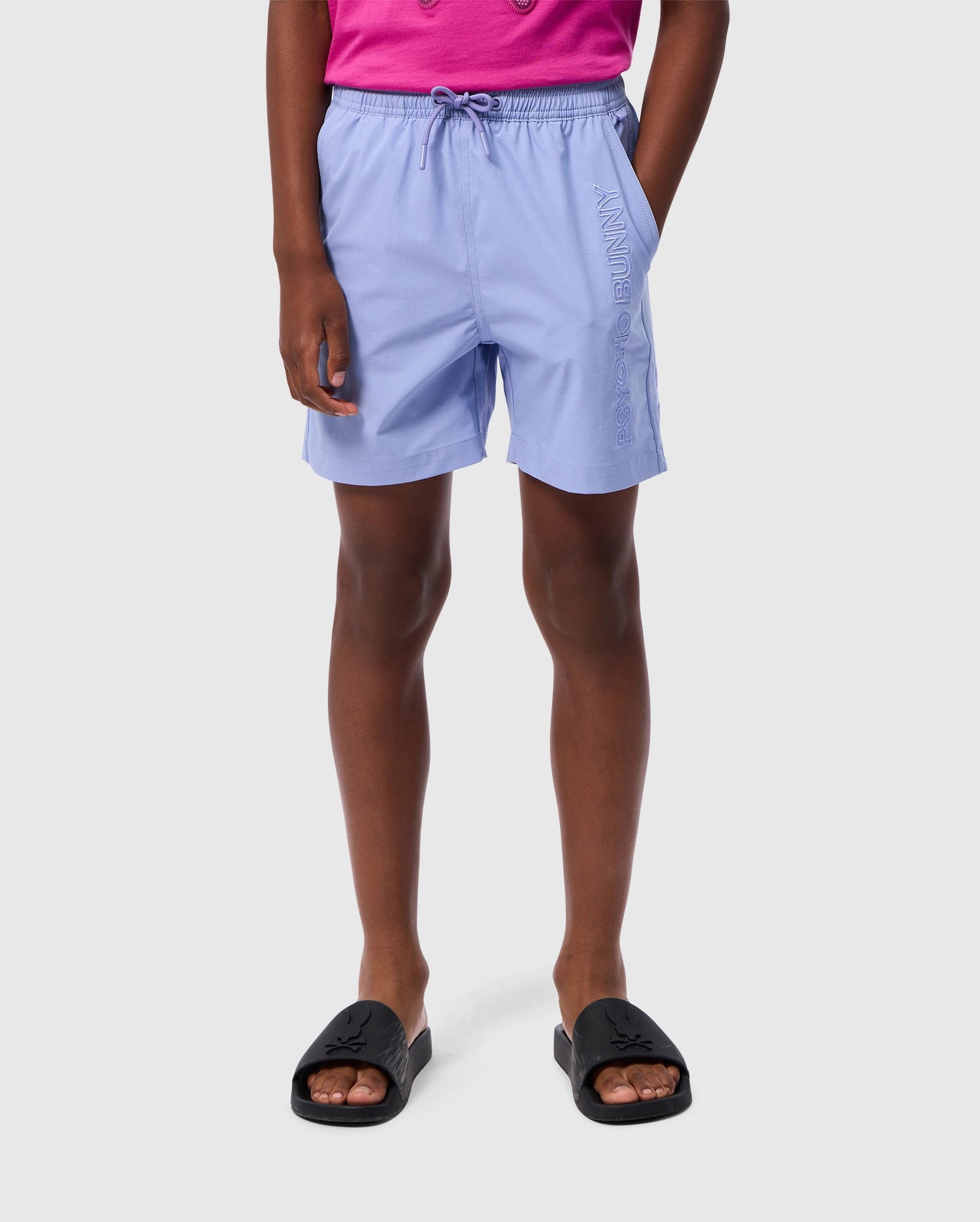 A person is wearing light purple KIDS MELVIN SWIM TRUNK - B0W665C200 by Psycho Bunny with a drawstring waist and the word 