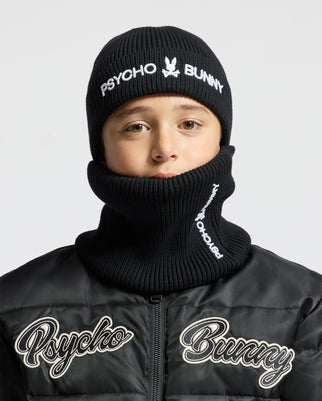 A person wearing a KIDS BEANIE AND NECKWARMER SET - B0X346E200 from Psycho Bunny, with the beanie and neck warmer partially covering their face, paired with a black jacket featuring "Psycho Bunny" embroidered on the chest. The background is plain white.