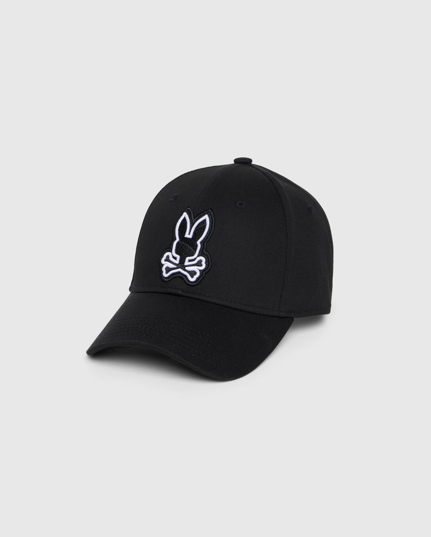 A black men's Lenox baseball cap featuring an embroidered white outline of a bunny head with crossed bones underneath on the front. Made from 100% cotton, it has a curved brim and an adjustable flip-clap fastening at the back. The Psycho Bunny MENS LENOX BASEBALL CAP - B6A122B2HT offers both style and comfort for everyday wear.