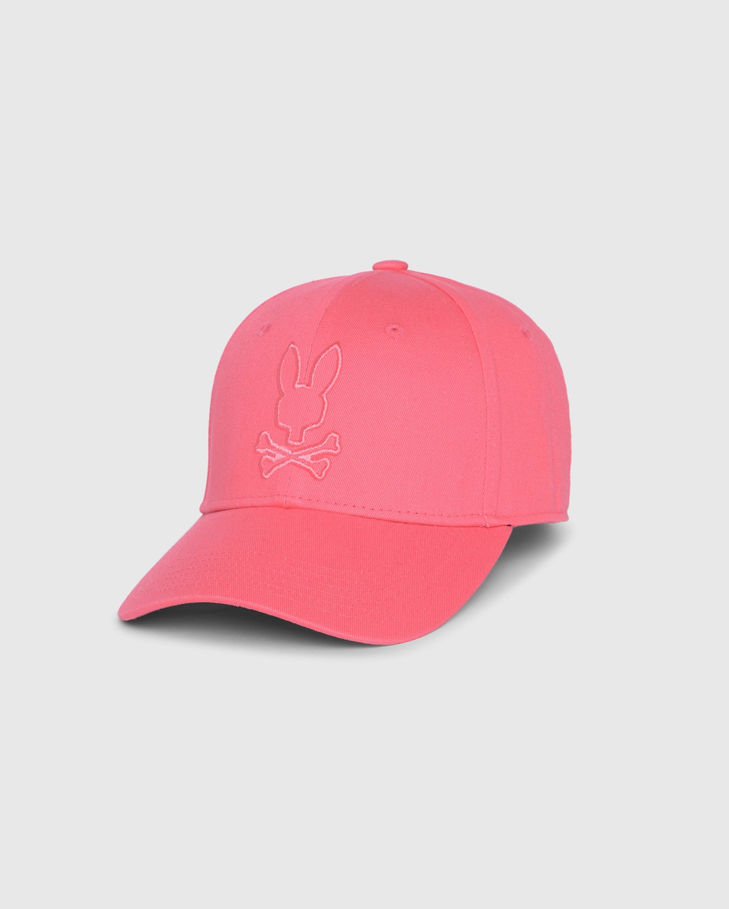 A bright pink MENS DANBY BASEBALL CAP - B6A360B2HT from Psycho Bunny with an embroidered bunny head above two crossed bones on the front panel. The cap features a curved brim, six ventilation holes on the crown, and an adjustable clasp for a perfect fit.