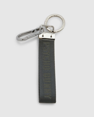 Introducing the WOVEN TAB KEYCHAIN - B6A374E200 by Psycho Bunny: a sleek and modern keychain featuring a silver metal clip and ring, connected to a green fabric strap with embossed text. The woven strap has metallic ends that securely attach it to the ring and clip, making it perfect for everyday carry.