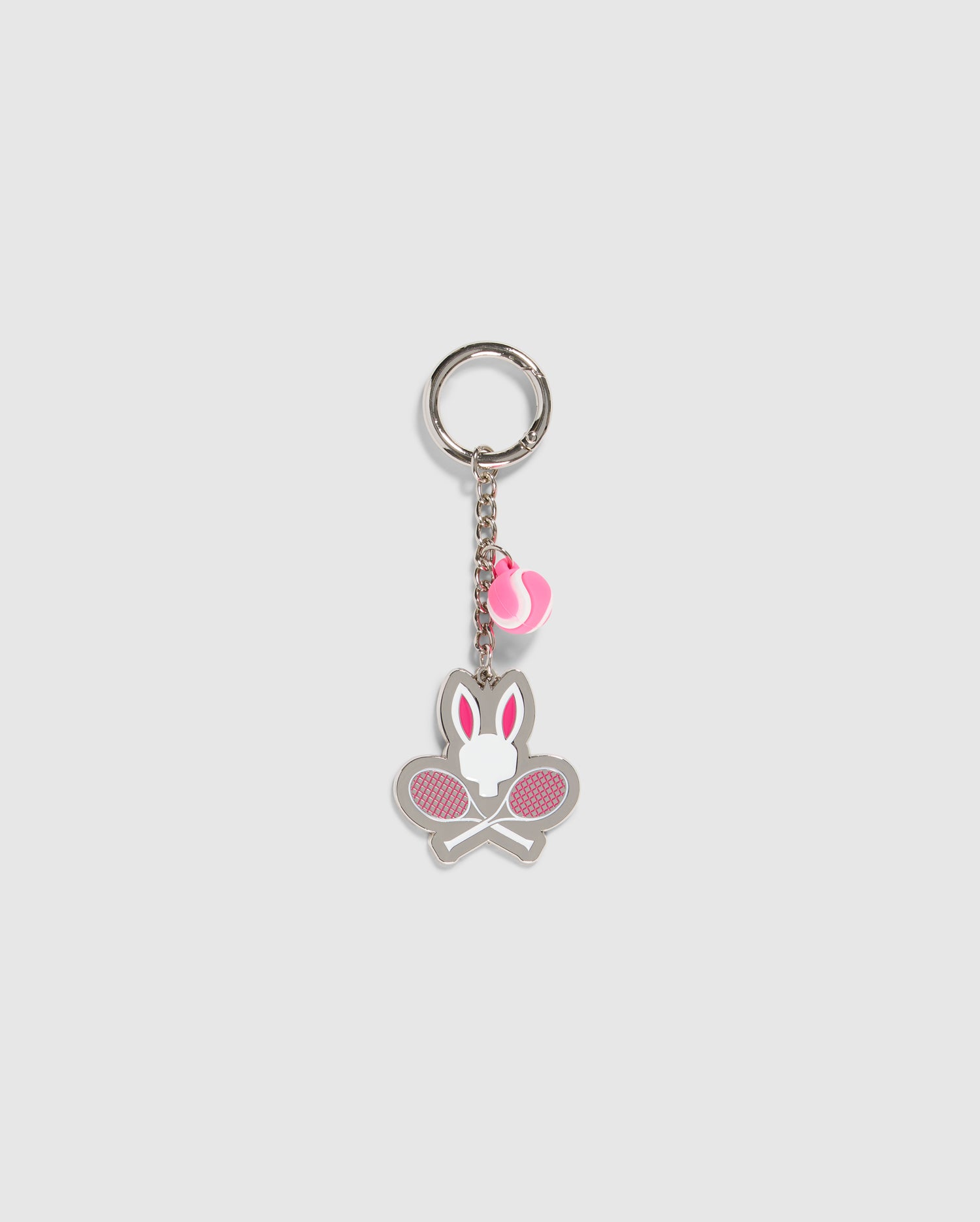A Psycho Bunny TENNIS KEYCHAIN - B6A657C200 featuring a silver ring connected to a chain. At the end, there's a charm with a stylized rabbit head above two crossed tennis rackets in white and pink. Another small pink tennis ball charm is also attached to the chain for added flair.