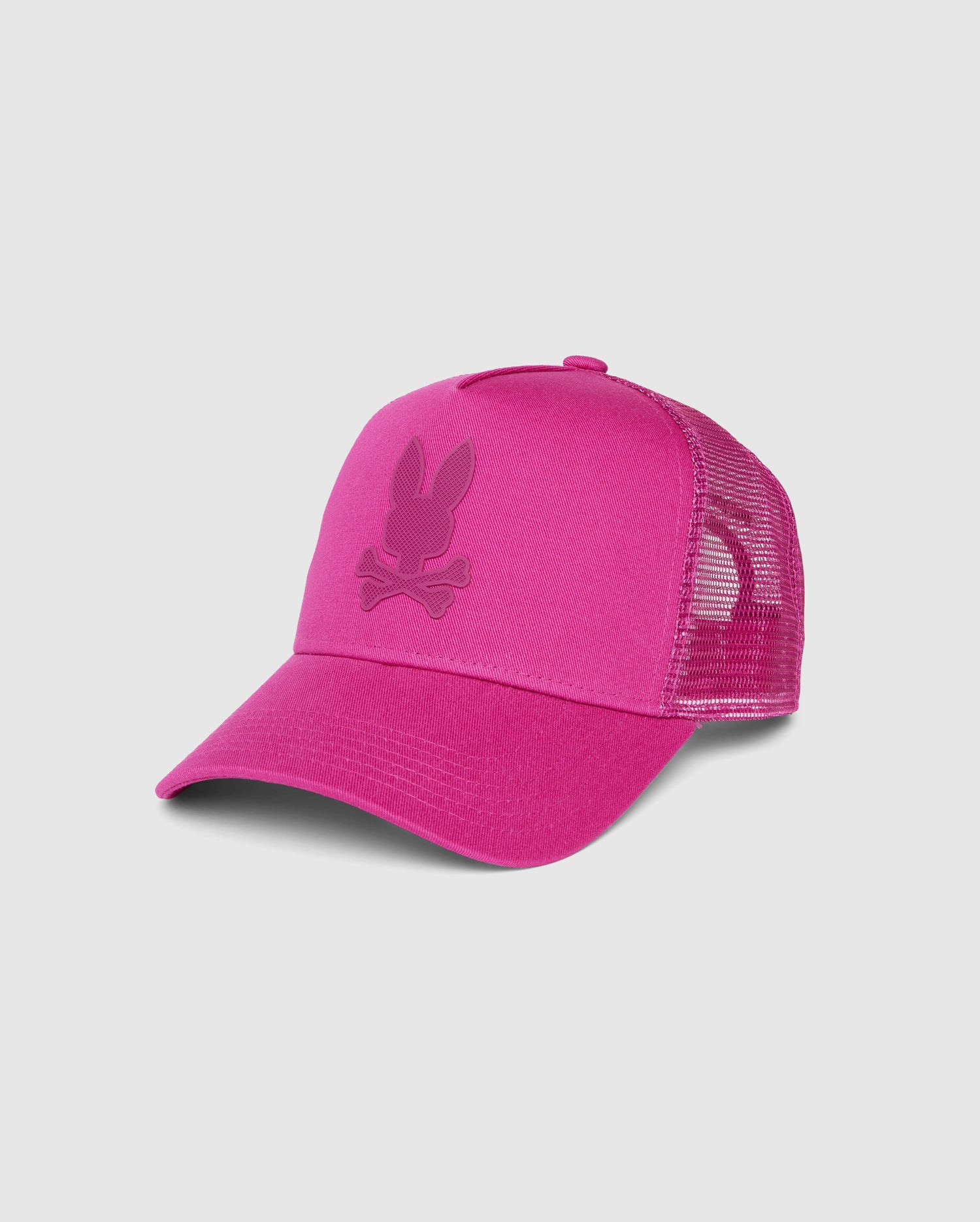 A vibrant pink MENS RIVIERA TRUCKER CAP - B6A667C200 featuring a mesh back for ventilation and an adjustable snapback fastening. The front panel displays an embroidered logo of a stylized bunny head with crossed bones underneath, evoking early 2000s nostalgia. This cap is from Psycho Bunny.