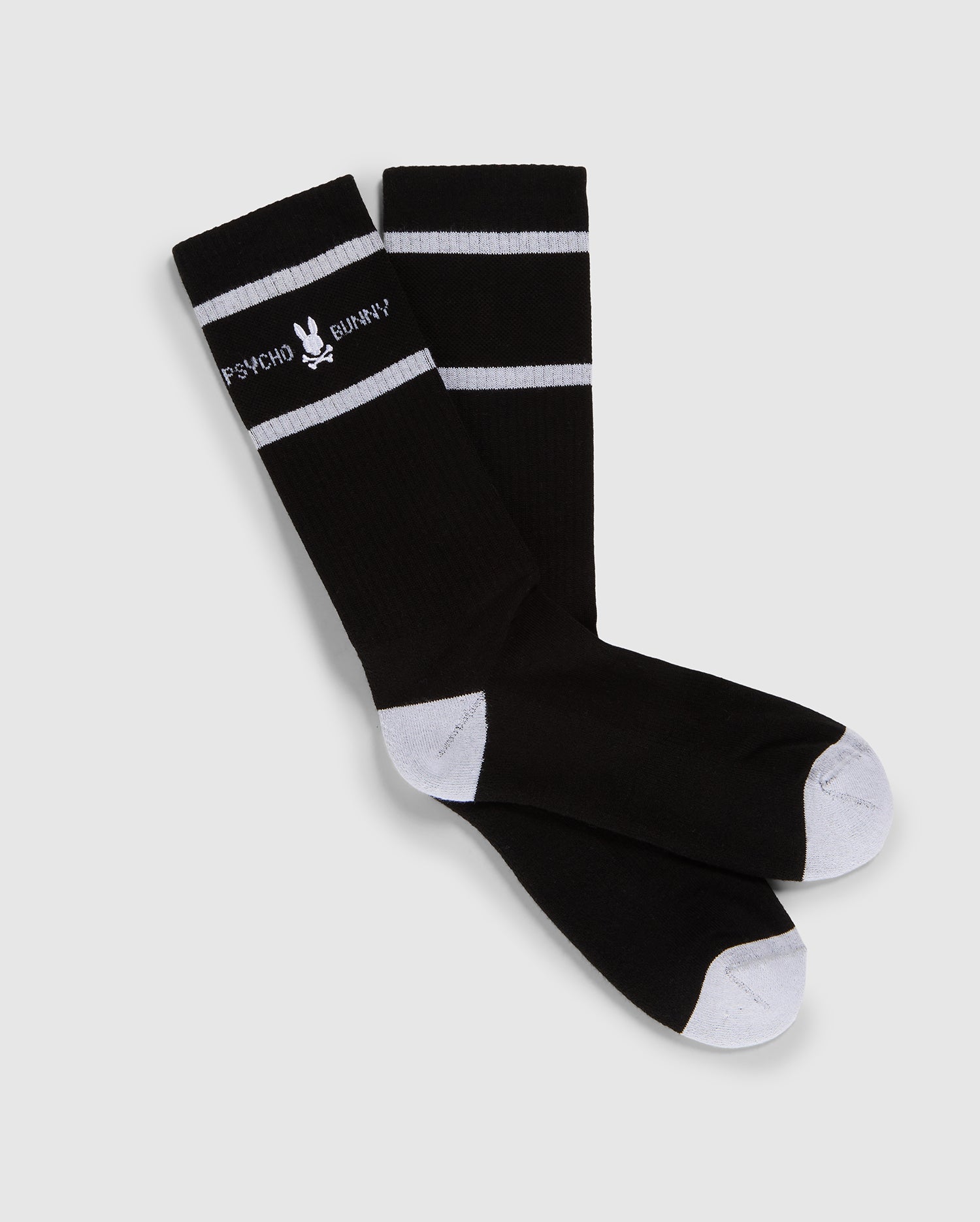 A pair of black knee-high Psycho Bunny fashion socks with white toe and heel patches and two white horizontal stripes near the top, featuring the text 