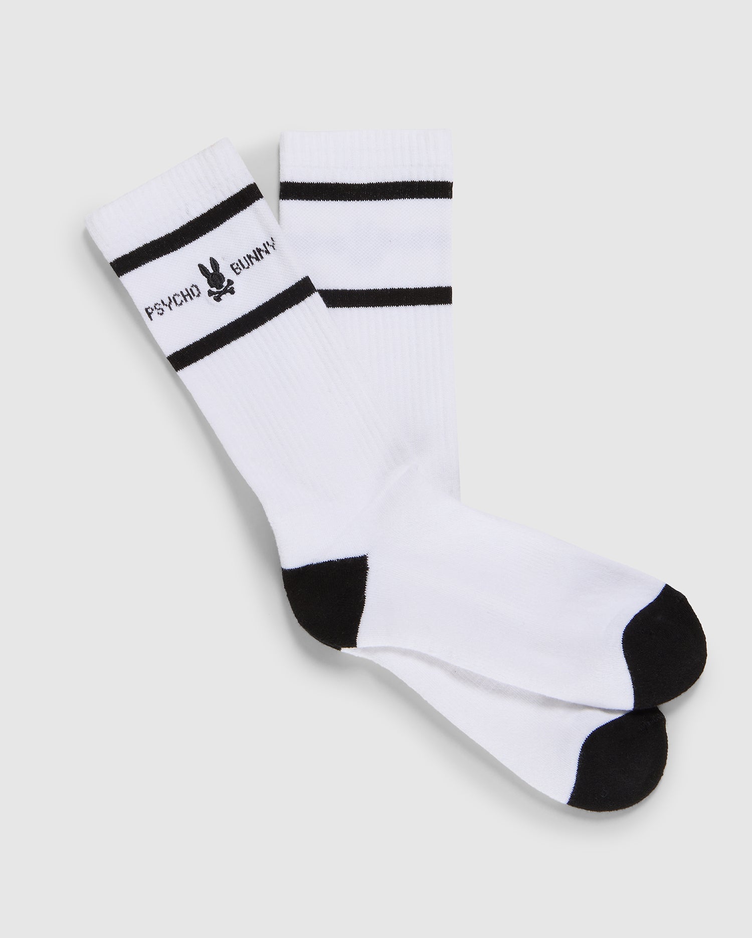 A pair of white crew socks with black toes and heels, made from Pima cotton, featuring two horizontal black stripes and a Psycho Bunny logo near the ribbed cuff on a plain background.