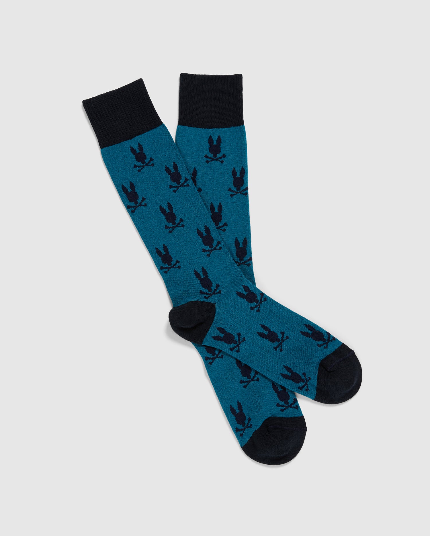 A pair of Psycho Bunny's MENS ALL OVER BUNNY DRESS SOCKS (B6F750D200) features an eye-catching design with a blue base, accented by black cuffs, heels, and toes. Adorned with a repeating pattern of dark bird silhouettes, the socks are crafted in Peru from a premium Pima cotton blend. They're displayed laid flat on a white background with one sock slightly overlapping the other.