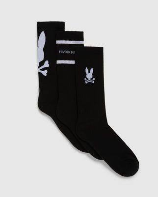 Displayed are three pairs of black sport socks from Psycho Bunny, known as the MENS 3 PACK SPORT SOCK - B6F997D200. Crafted from luxurious Peruvian pima cotton, each pair showcases a unique white design: one with a large bunny skull motif near the top, another featuring "PSYCHO BUNNY" text and horizontal stripes, and the last with a small bunny skull and crossbones near the top.