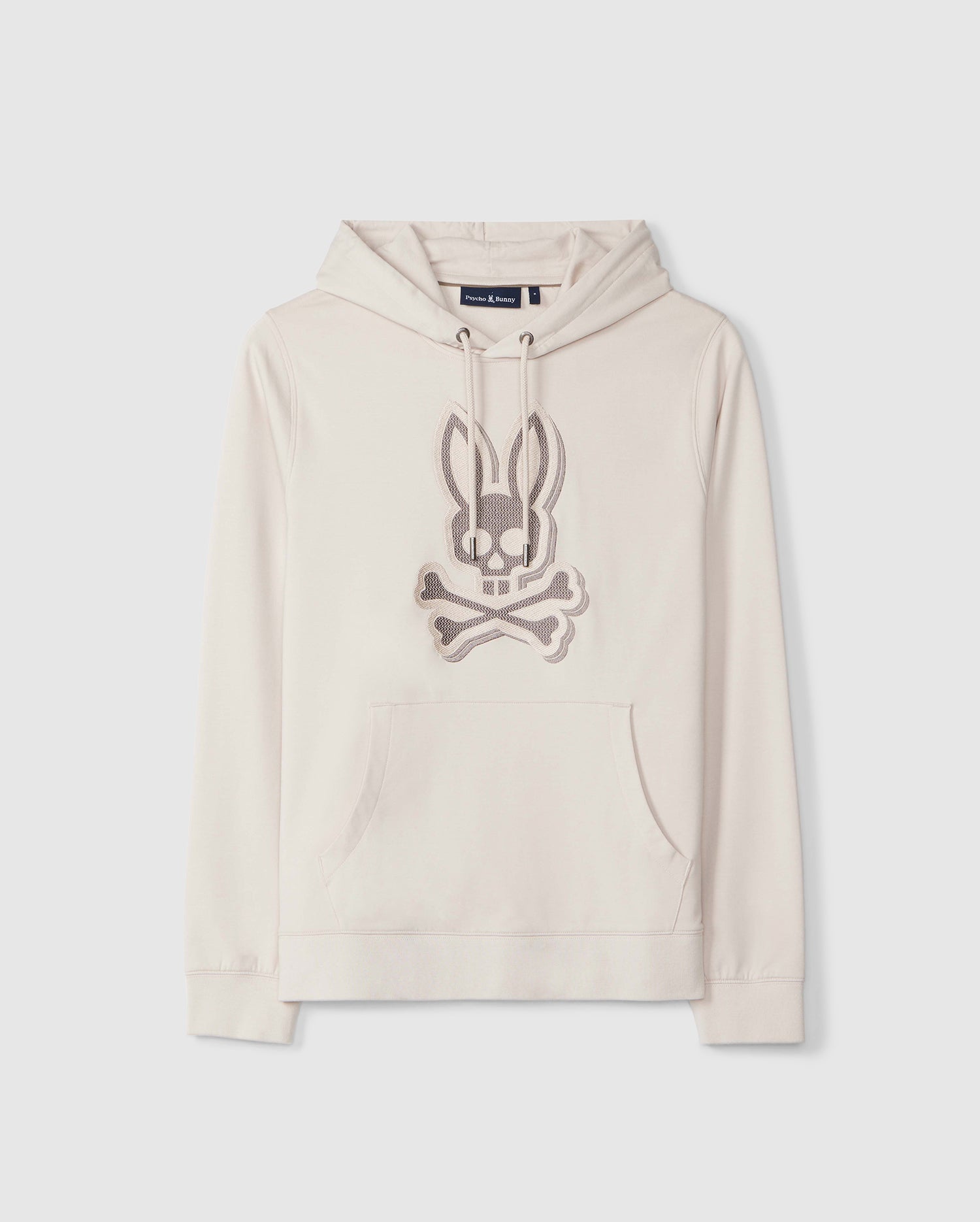 A cream-colored Psycho Bunny MENS LIVINGSTON PULLOVER HOODIE - B6H246B200 with a front pouch pocket, featuring an embroidered Bunny-design of a rabbit head and crossed bones in light brown thread. The hoodie is crafted from micro French terry.