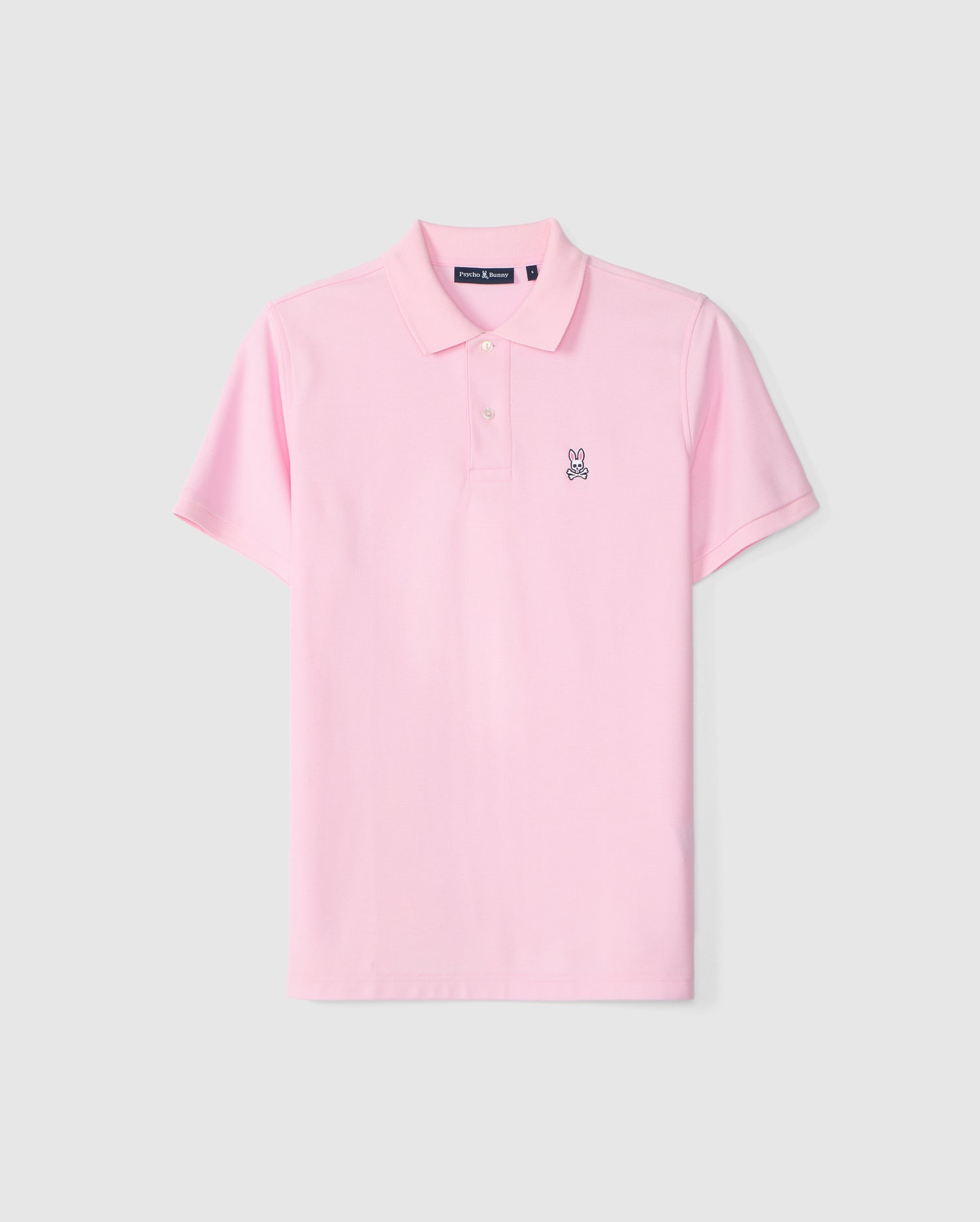 The Psycho Bunny MENS CLASSIC PIQUE POLO SHIRT - B6K001CRPC is a pale pink, short-sleeved polo shirt with a collar and two white buttons. Crafted from luxurious Peruvian Pima cotton, this classic pique polo features a small embroidered rabbit emblem on the left chest. The shirt is displayed against a plain light gray background.