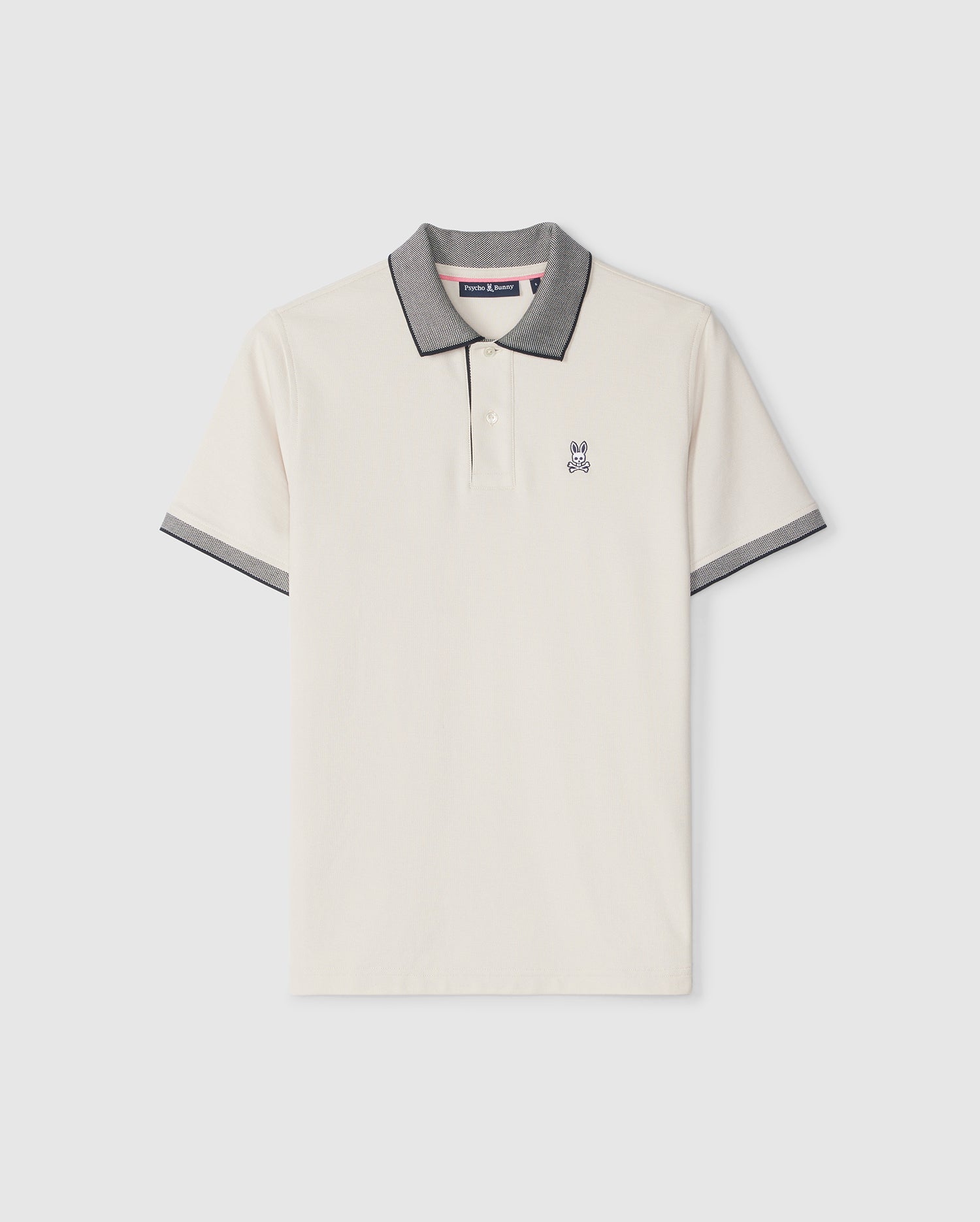 A cream-colored Psycho Bunny men's Southport pique polo shirt with a gray collar and sleeve trim, featuring a small embroidered logo on the left side of the chest. The shirt is displayed against a plain light background.