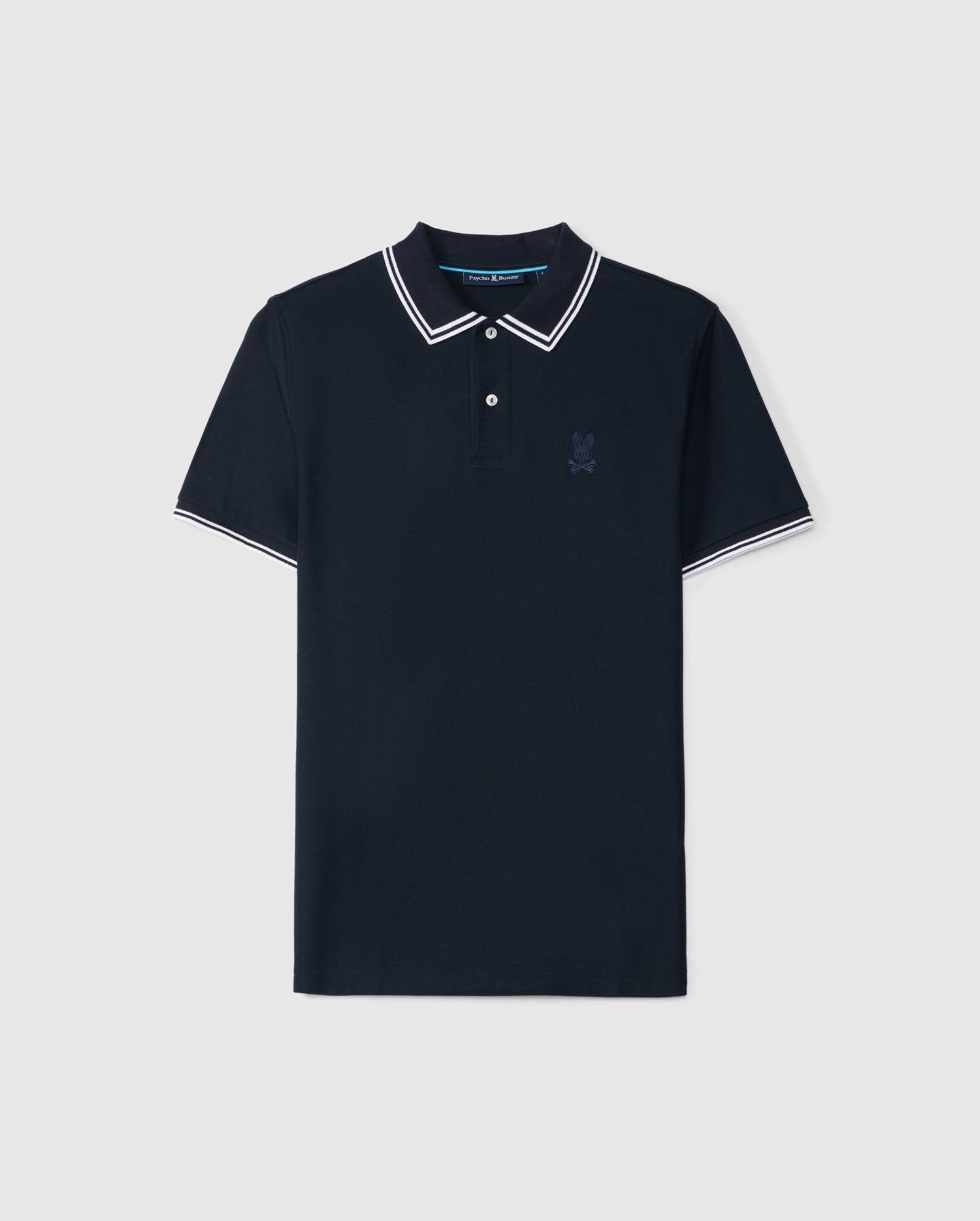 A navy blue Psycho Bunny MENS BELTON PIQUE POLO - B6K575C200 with contrasting tipping on the collar and sleeves. The shirt features a three-button placket and an embroidered Bunny logo on the left chest, set against a plain, light grey background.
