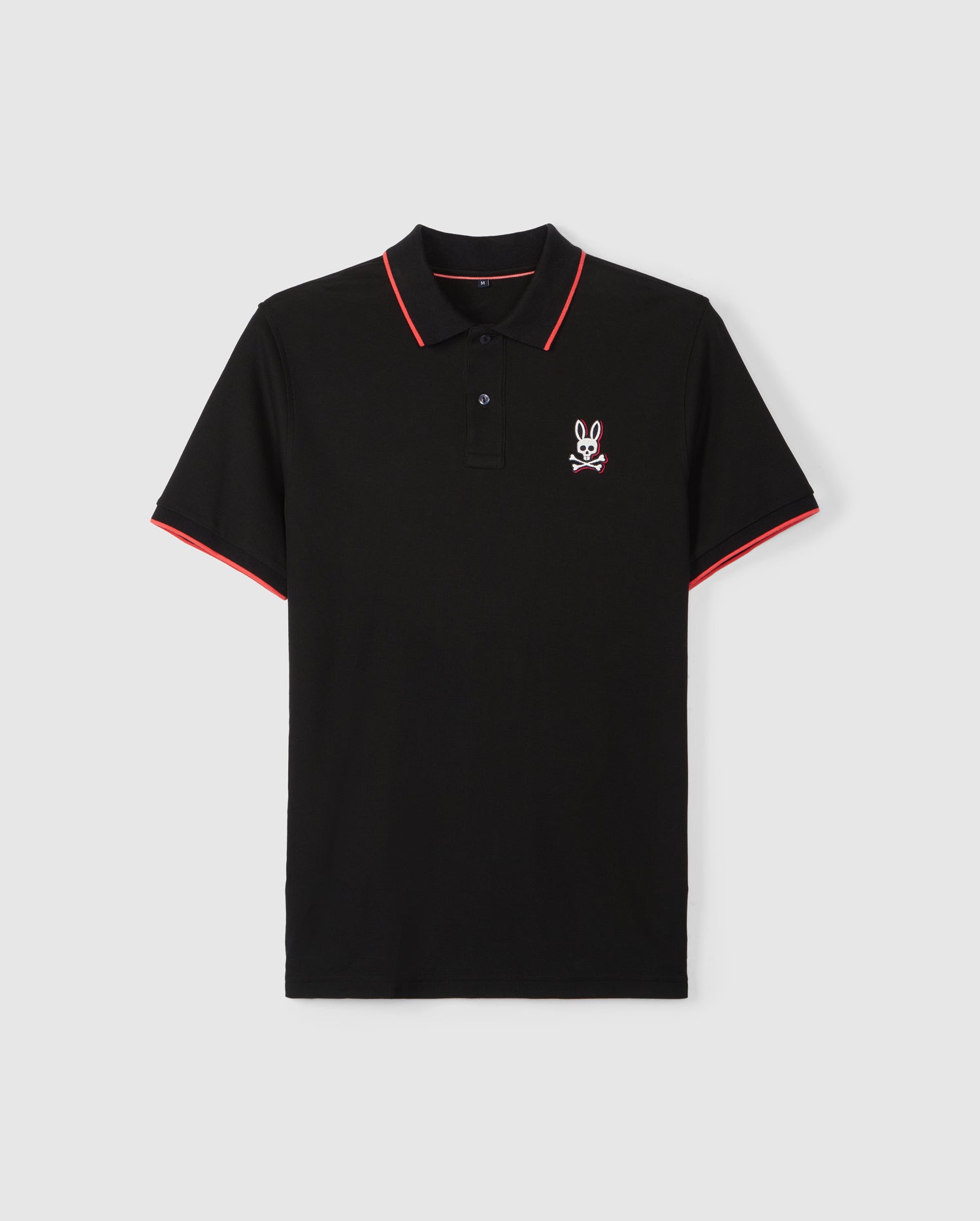 A black short-sleeve polo shirt crafted from Pima cotton piqué, featuring red trim on the sleeve cuffs and collar. It has a buttoned placket and an embroidered tonal Bunny logo with crossbones on the left chest. The MENS KAYDEN PIQUE POLO - B6K675C200 by Psycho Bunny is displayed against a plain white background.