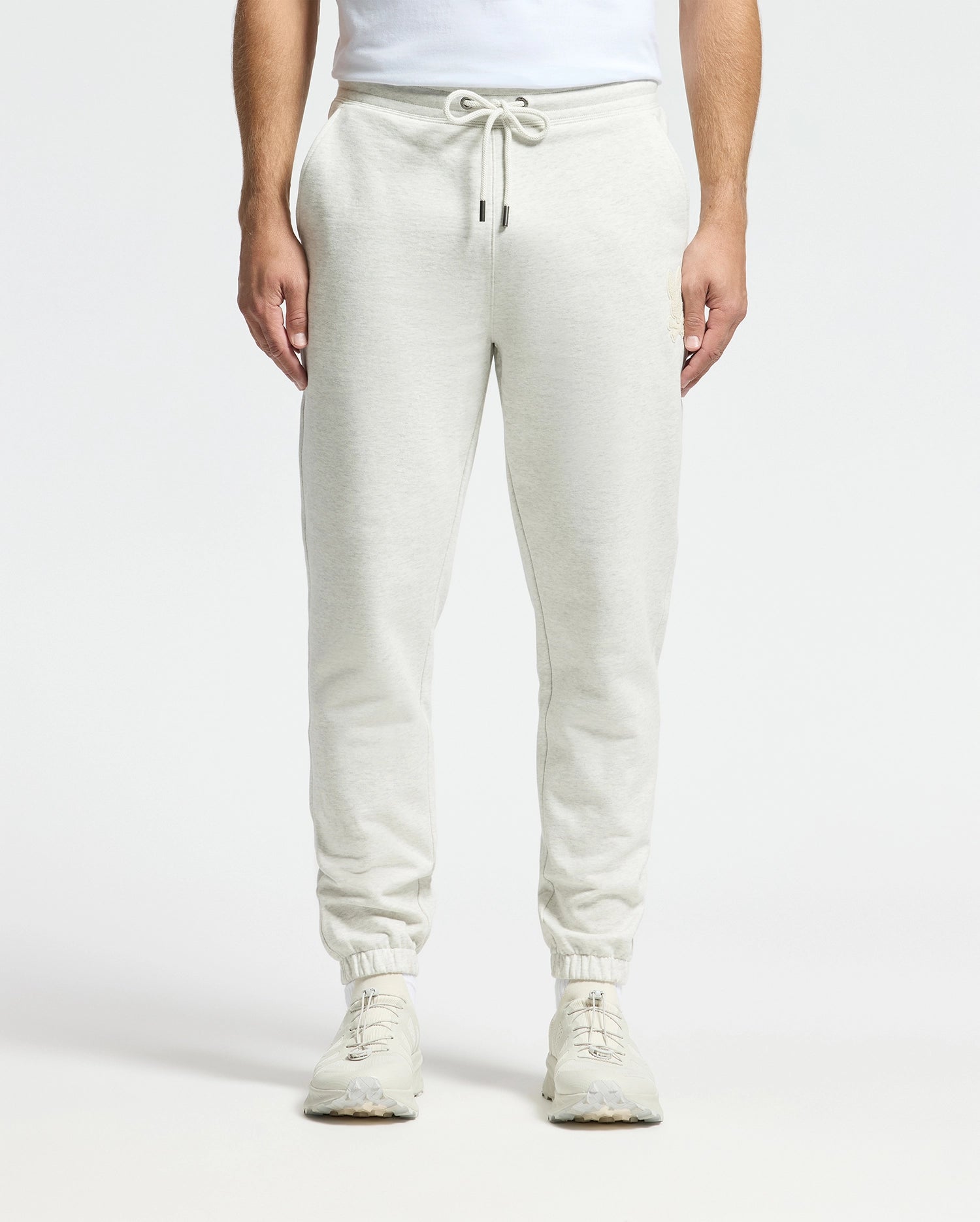 Dressed in Psycho Bunny's Mens Eldorado Brush Back Jogger (B6P285E200) in light gray with a drawstring waist, paired with white sneakers. The Jogger's brushback cotton ensures comfort, set against a plain white background.