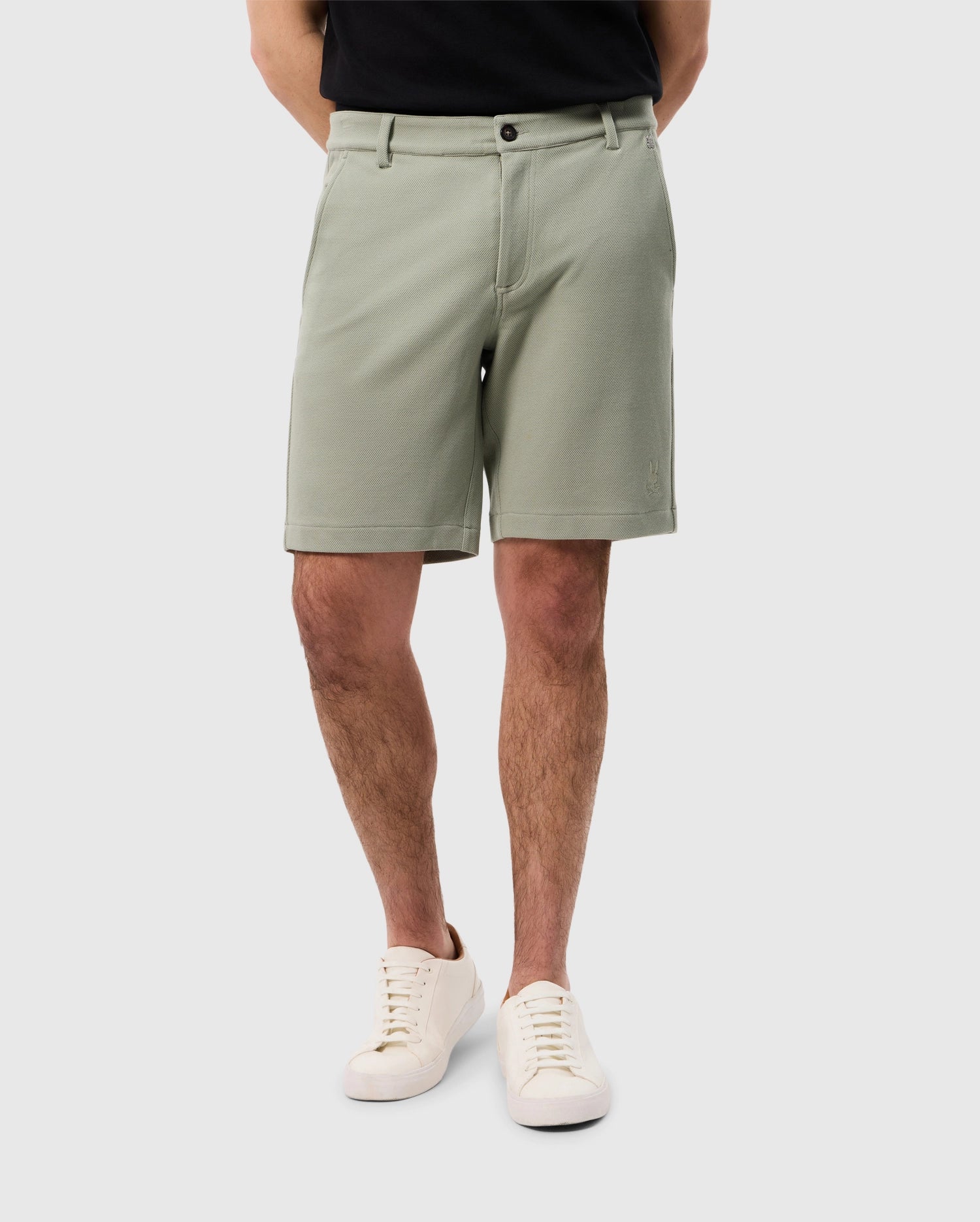 A man wearing Psycho Bunny's MENS SHIRO KNIT HONEYCOMB SHORT - B6R567C200 and white sneakers stands with his back to the camera, focusing on the lower half of his body against a plain background.