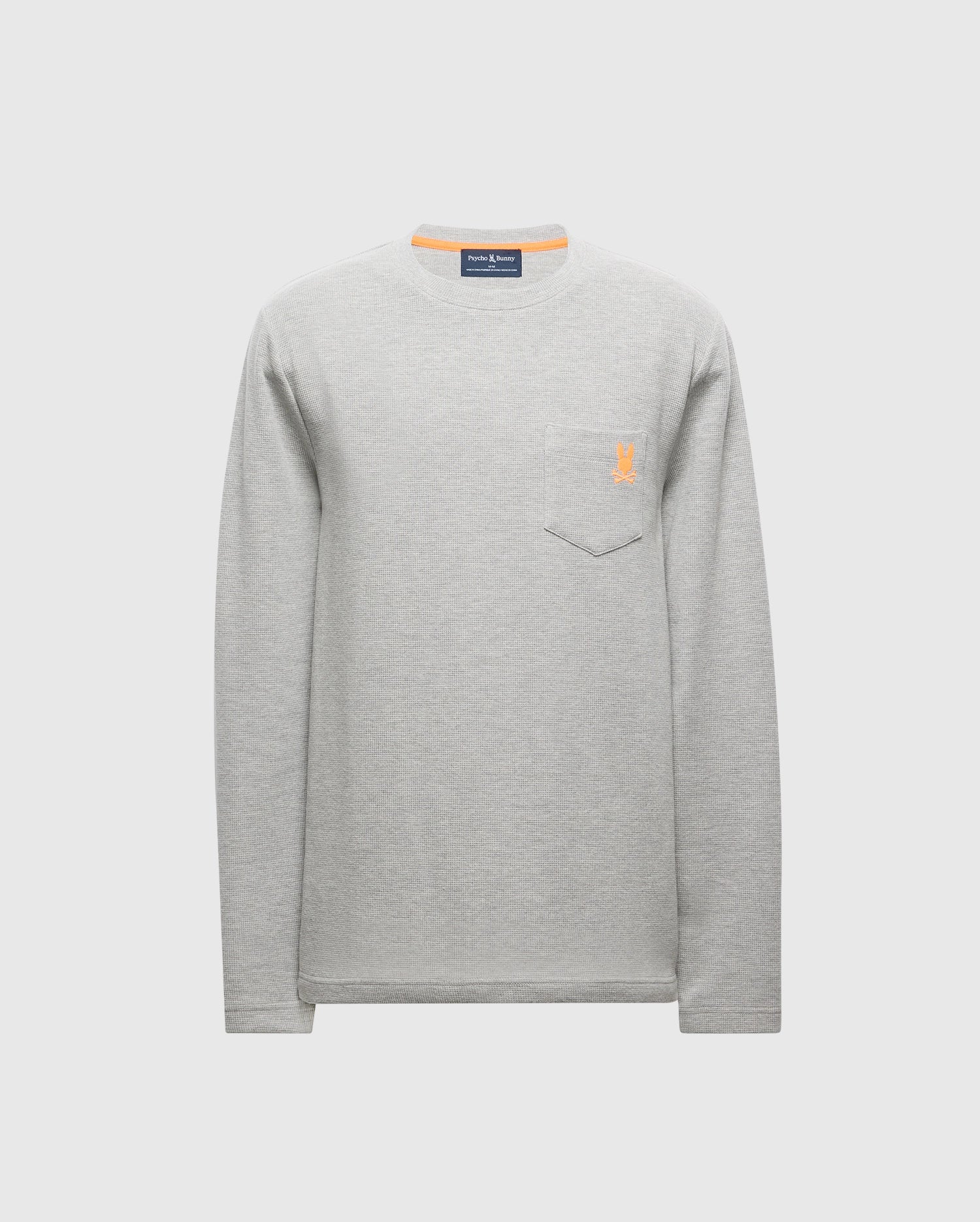 The Psycho Bunny MENS VAIL WAFFLE LOUNGE LONG SLEEVE TEE - B6T672E200 is a stylish men's light gray waffle knit tee with a crew neckline and a chest pocket on the left side. It features a small orange embroidered logo and is displayed on a plain white background.