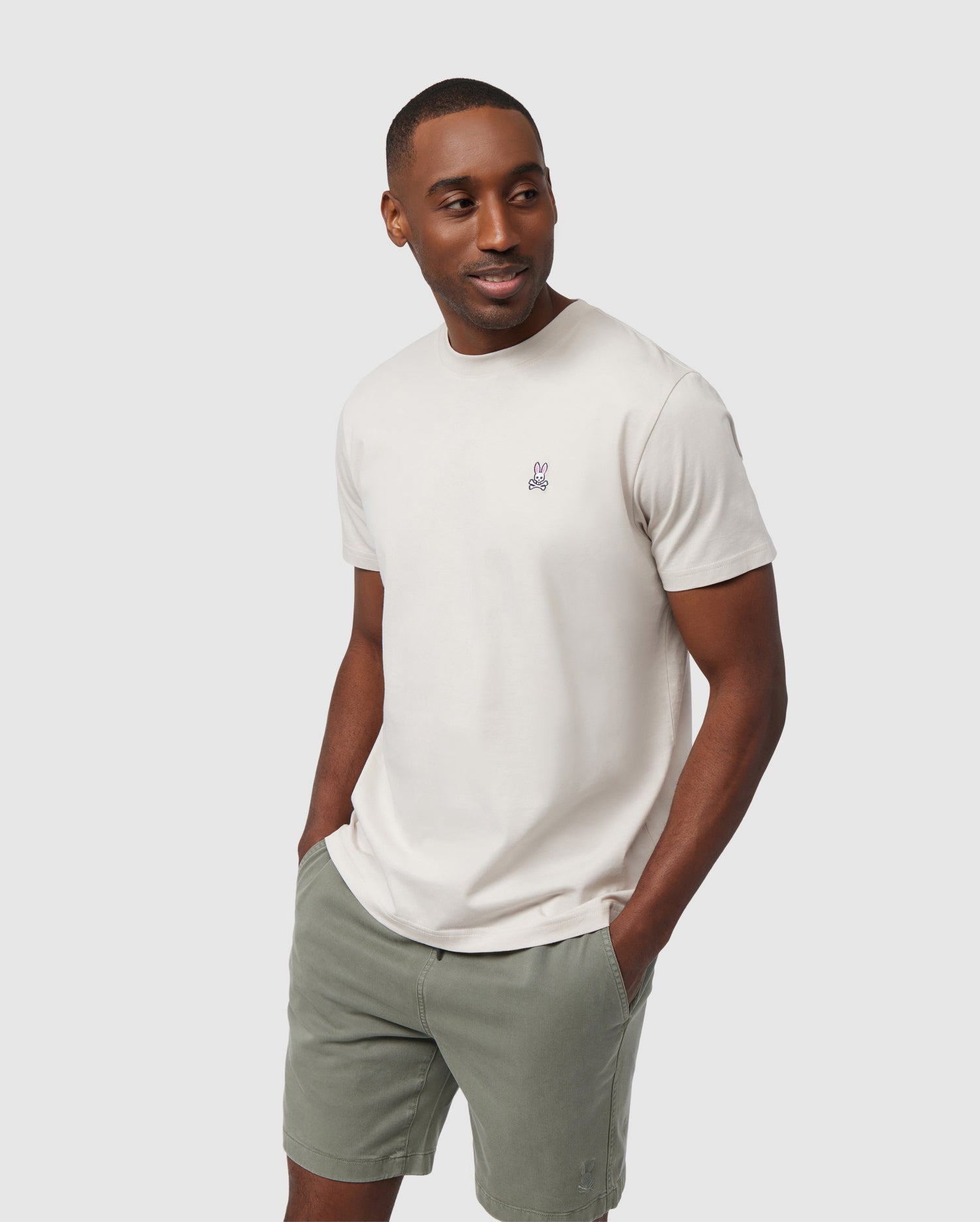 A man in a casual pose wearing a Psycho Bunny MENS CLASSIC CREW NECK TEE with a small logo on the chest and olive green shorts, against a plain white background.