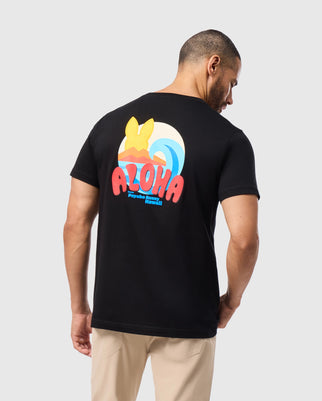 A man wearing a Psycho Bunny MENS HAWAII CITY TEE - B6U169Y1PC in black Pima cotton, adorned with "Aloha" and a yellow hat design on the back, stands against a light gray background. He is facing away, showcasing the men's T-shirt's vibrant text and imagery.