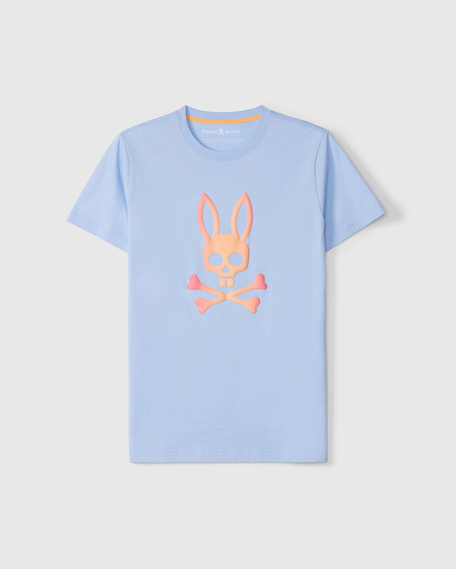 A light blue short-sleeve graphic tee featuring a stylized bunny skull and crossbones design in the center. The graphic, showcasing an ombre effect in peach and pink, is printed on luxurious Peruvian Pima cotton. The **Psycho Bunny MENS NORWOOD GRAPHIC TEE - B6U311B2TS** is displayed on a plain white background.