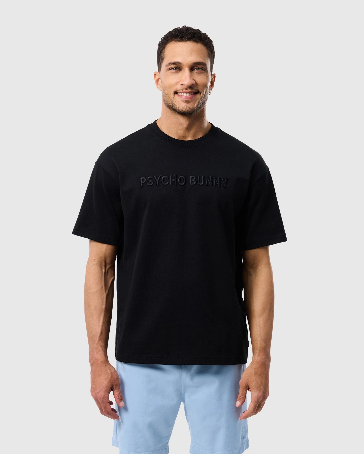 A man smiling at the camera, wearing a black Psycho Bunny Pima cotton tee with an embroidered 