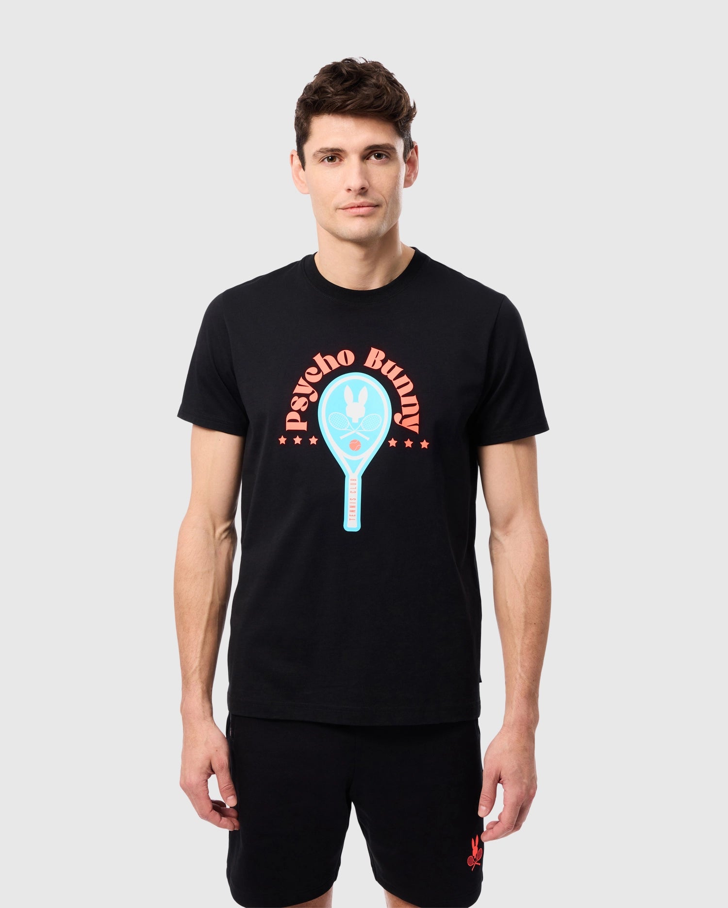 A man stands against a plain white background wearing a black MENS COURTSIDE GRAPHIC TEE - B6U682C200 with a colorful tennis-inspired Bunny logo and the words 