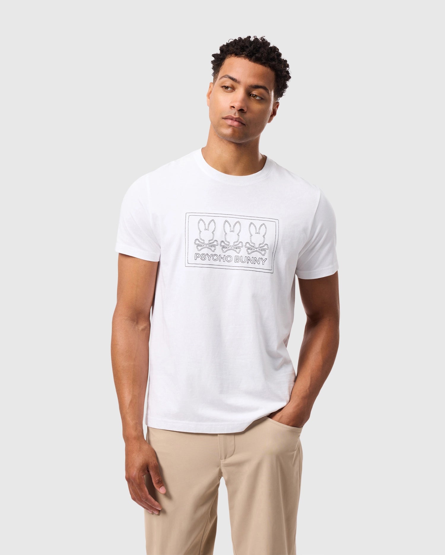 A man wearing the Psycho Bunny MENS TACOMA GRAPHIC TEE - B6U909D200, which features a rectangular logo with three bunny illustrations and the text 