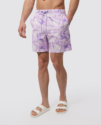 A man wearing a pair of Psycho Bunny MENS HEMPSTEAD SWIM TRUNK - B6W111Y1PO swim trunks and white sandals, standing against a white background. Only the lower half of his body is visible.