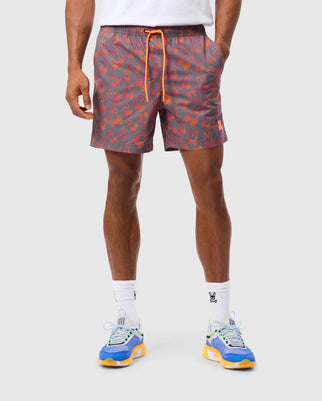 A person is wearing Psycho Bunny MENS SHELDON ALL OVER PRINT SWIM TRUNKS in gray, patterned with small red bunnies, a white shirt, and calf-length socks featuring the Psycho Bunny logo. They are also wearing colorful sneakers in blue, yellow, and white. The quick-dry fabric of the bunny-patterned outfit makes it perfect for any casual outing.