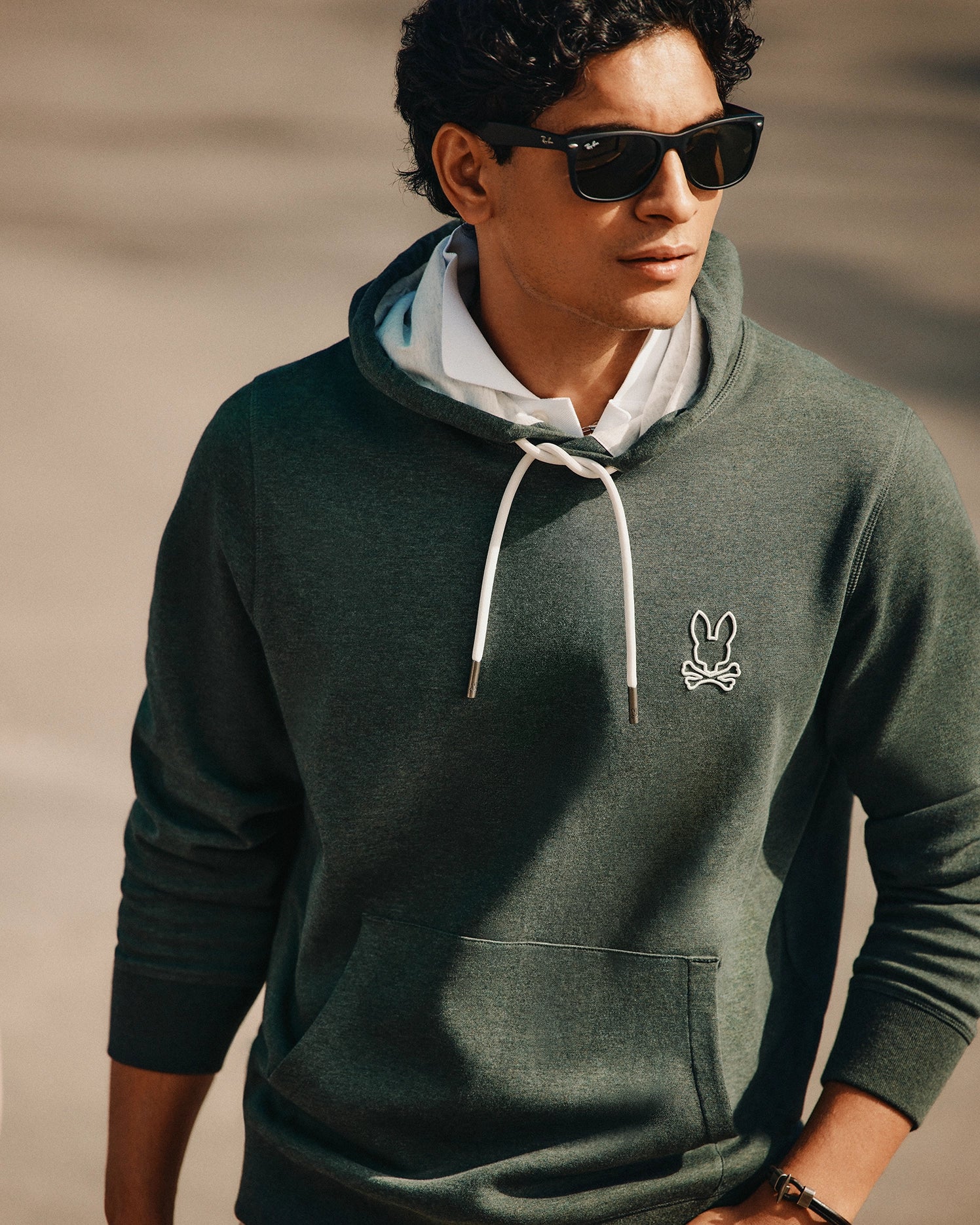 A person wearing sunglasses and the trendy Psycho Bunny MENS JAMES PREMIUM HOODIE - B6H789D200, featuring a white drawstring and a small embroidered logo on the chest. The individual is looking to the side while standing outdoors in a relaxed pose.