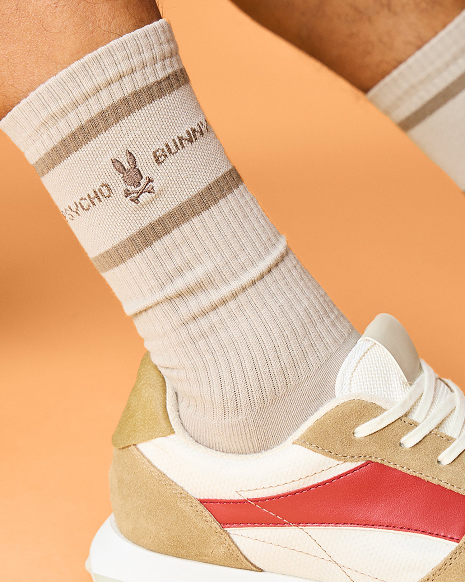 Close-up of a person's foot wearing a beige, Pima cotton-blend sock with an embroidered cartoon bunny logo and the text 